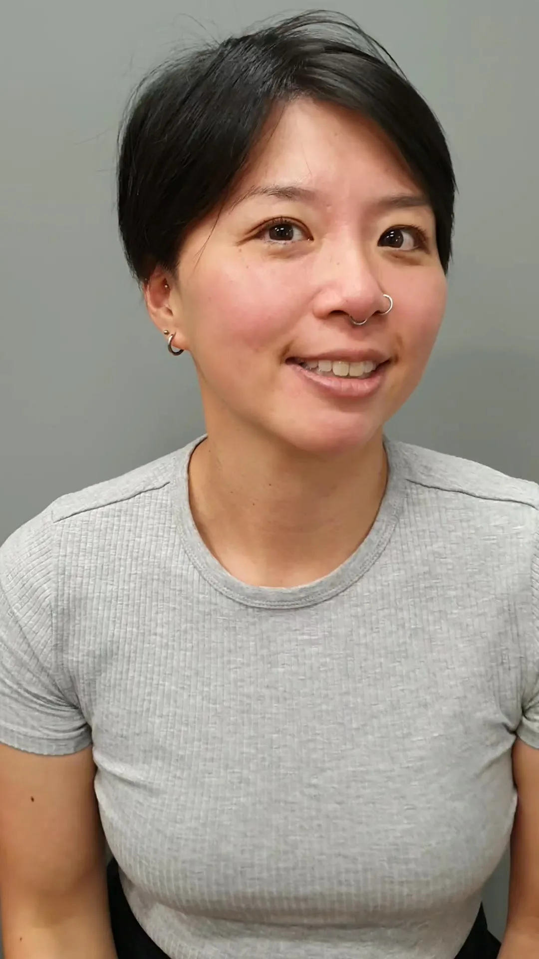 Dark pixie crop, client smiling, grey salon wall